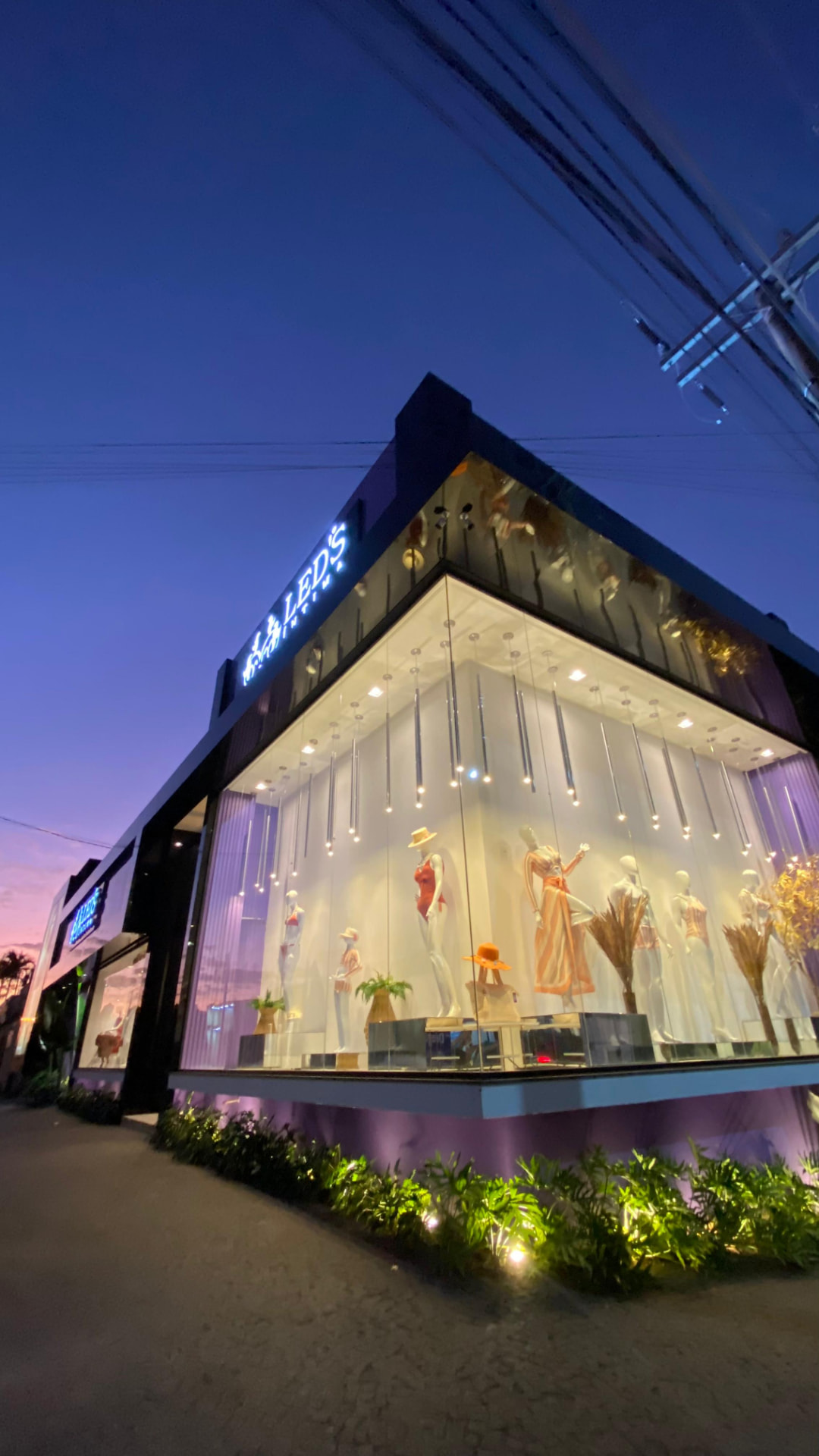 Loja Led's Íntima iluminada ao anoitecer, com vitrine de manequins